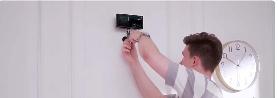 Person installing a Photon Matrix Mosquito Defensive system on a white wall with a clock in the background