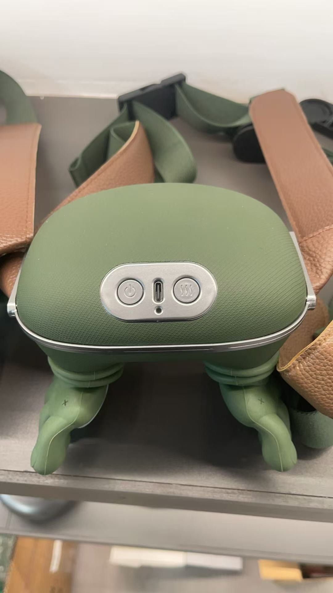 Green electronic neck massager with buttons on a metal surface